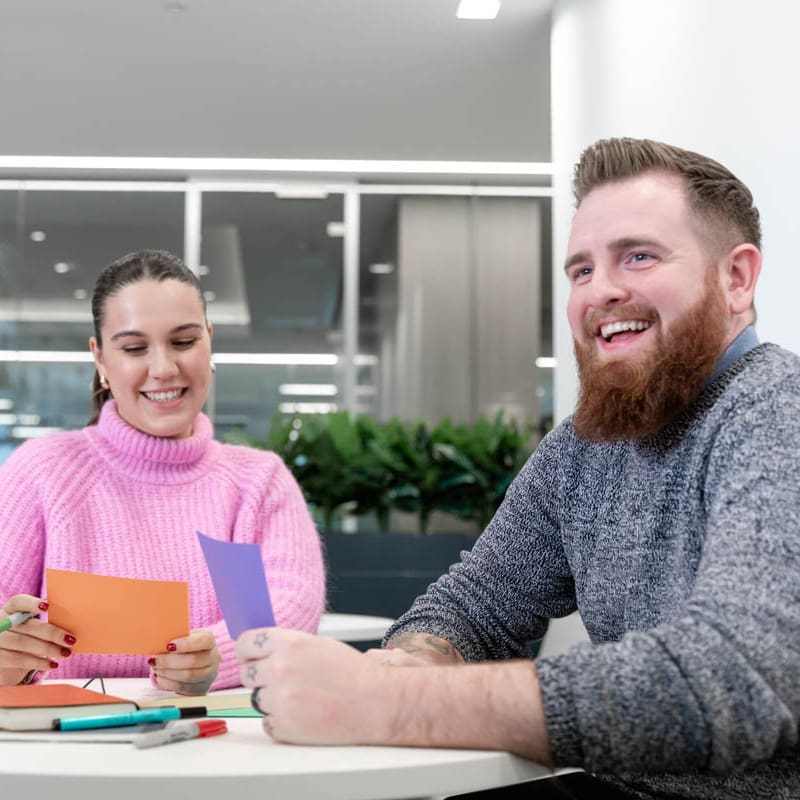 Two cheerful colleagues sit at a table looking a notes