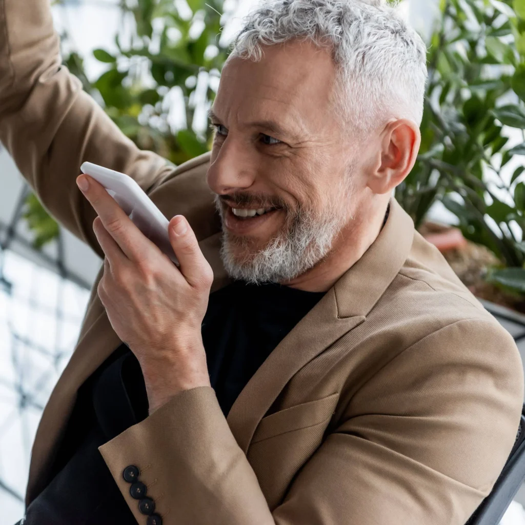 Cheerful businessman recording voice message near plants