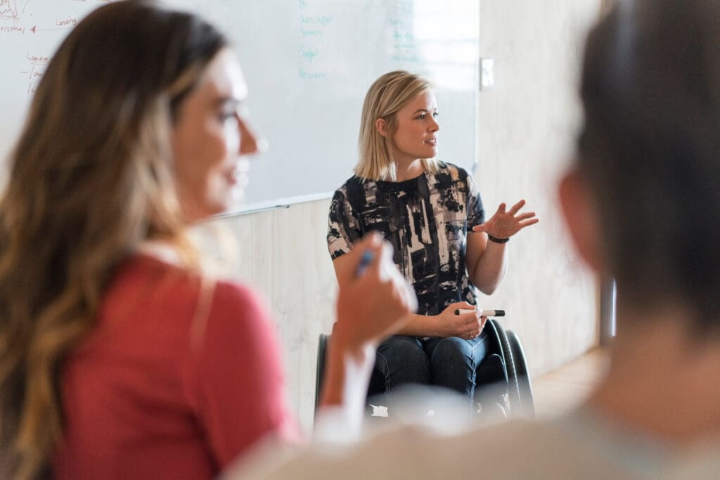 A woman in a wheelchair presents a meeting and writes on a whiteboard