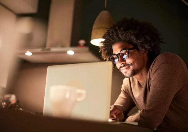 A man looks at his laptop in a dimly lit kitchen