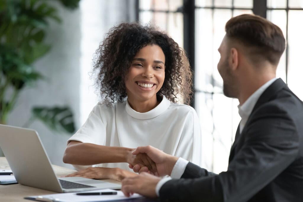 A women smiles at a man while shaking his hand