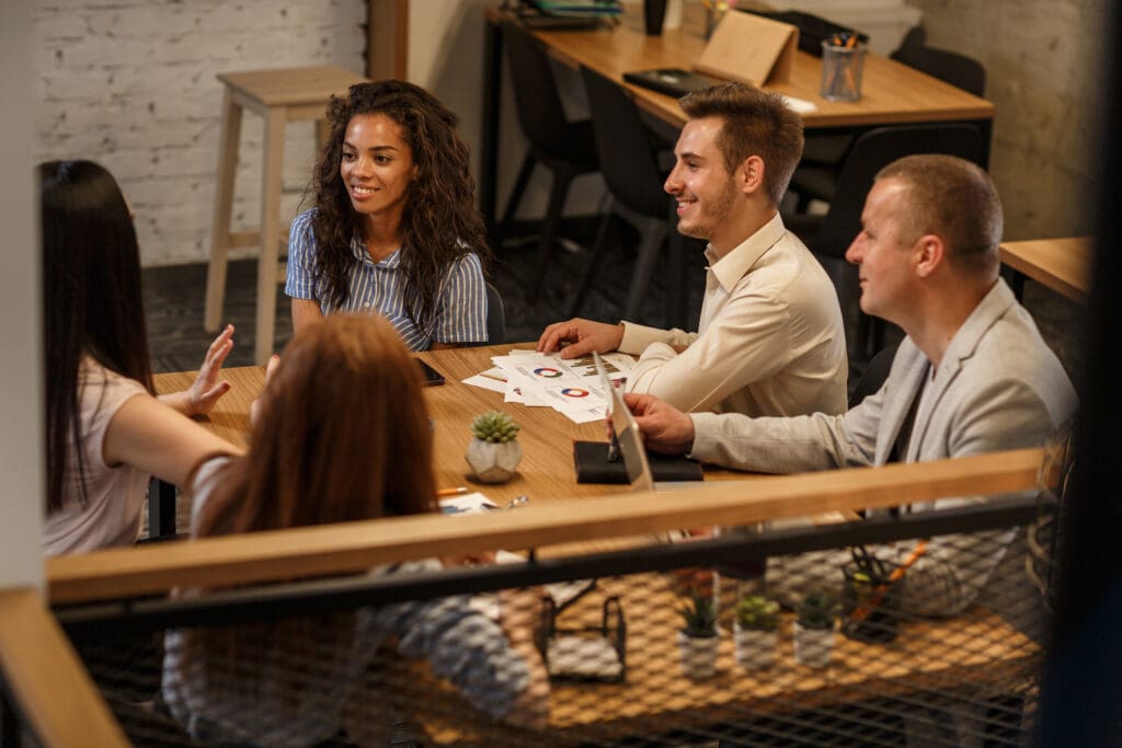 A group sit round a table with laptops and charts on paper