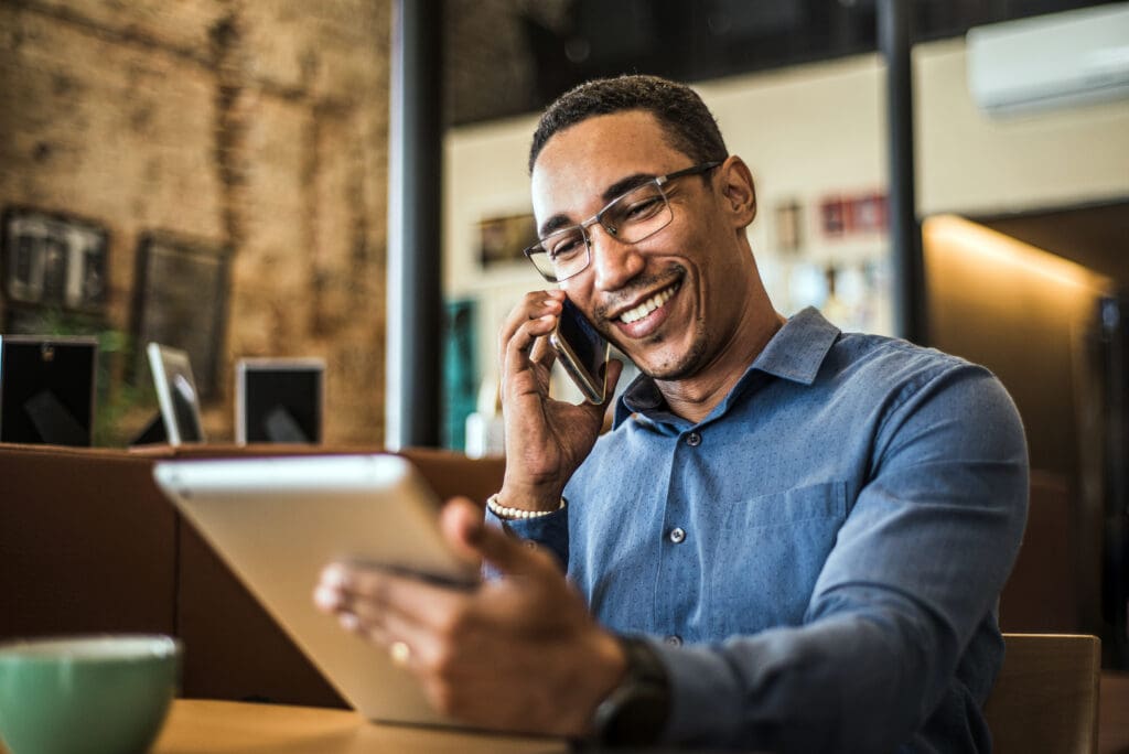 A man smiles while having a conversation on the phone and looking at a tablet screen