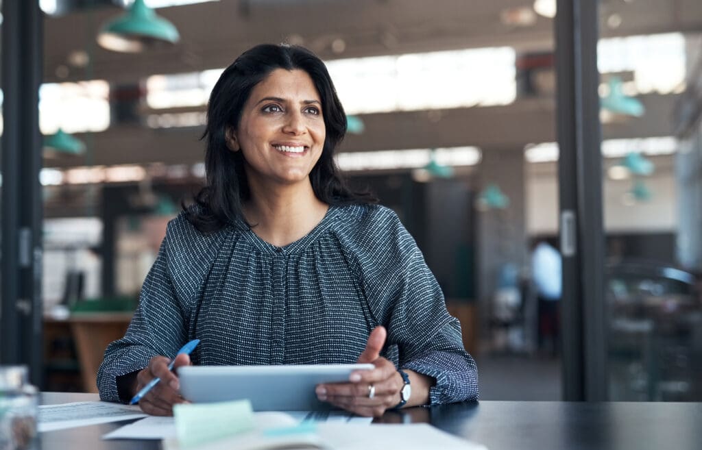 A women smiles as she holds a tablet in a modern workplace