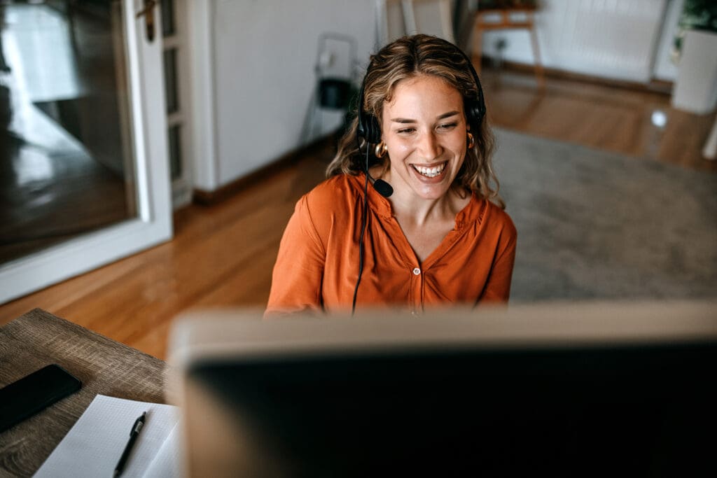 A man smiles at a computer screen wearing a headset