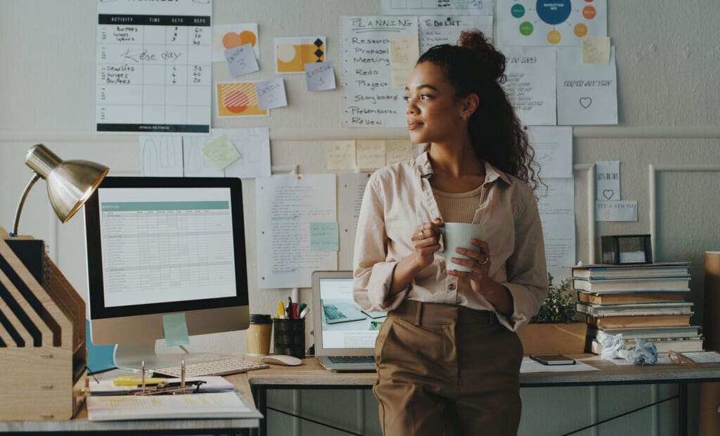 A woman looks away thoughtfully in front of her desk with organised notes and books