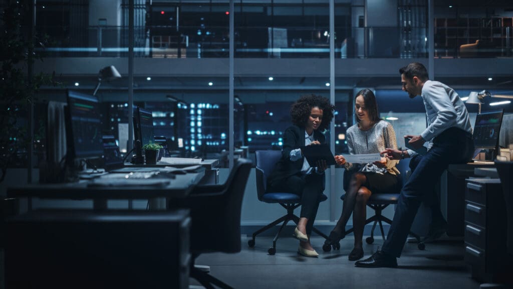 Two women and a man look at charts on paper in a modern office