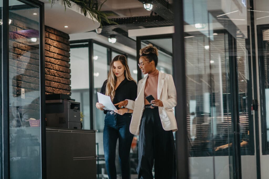 Two women look at a sheet of paper while walking