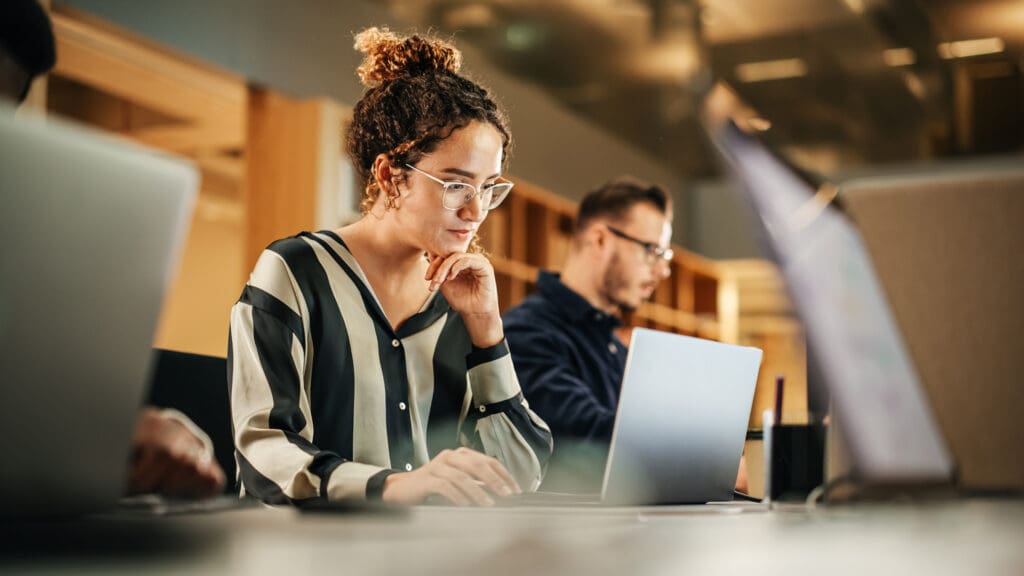 A woman looks thoughtfully at her laptop screen