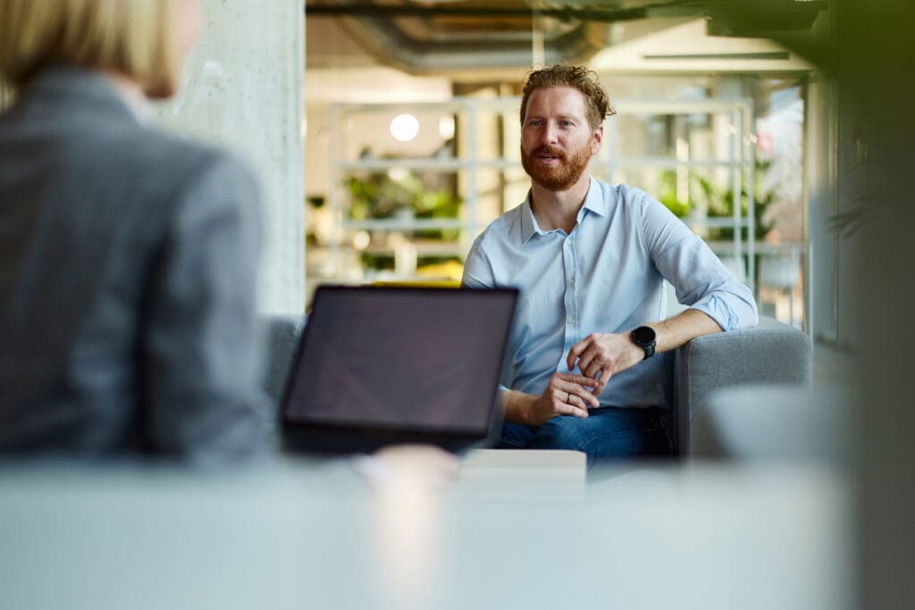 A man has a conversation with a woman while she looks at a laptop screen