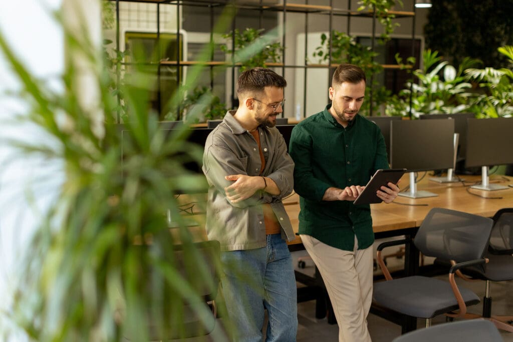 Two men look at a tablet screen in a verdant workplace