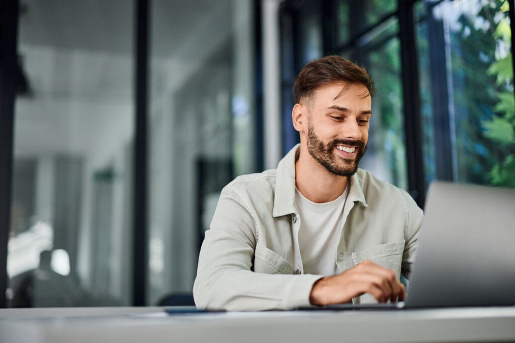 A young man smiling at his laptop