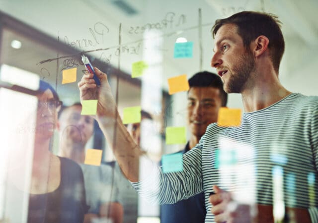 A group gathers around a man writing on a glass wall