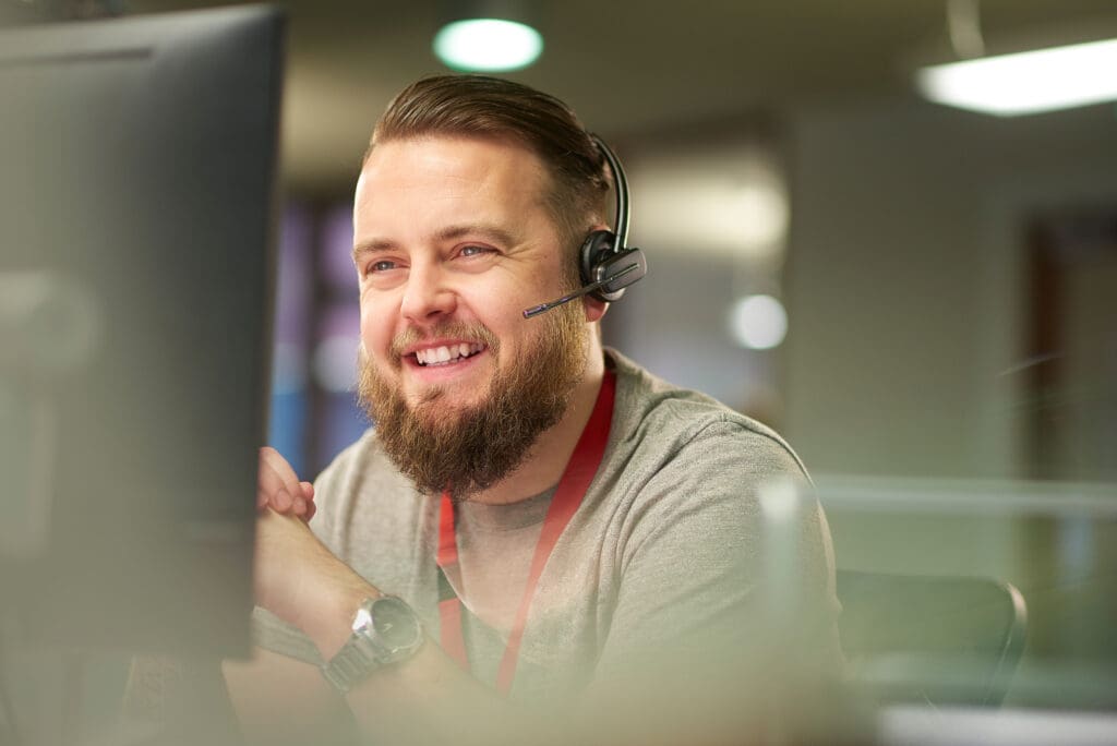 A man wearing a headset smiles at a computer screen