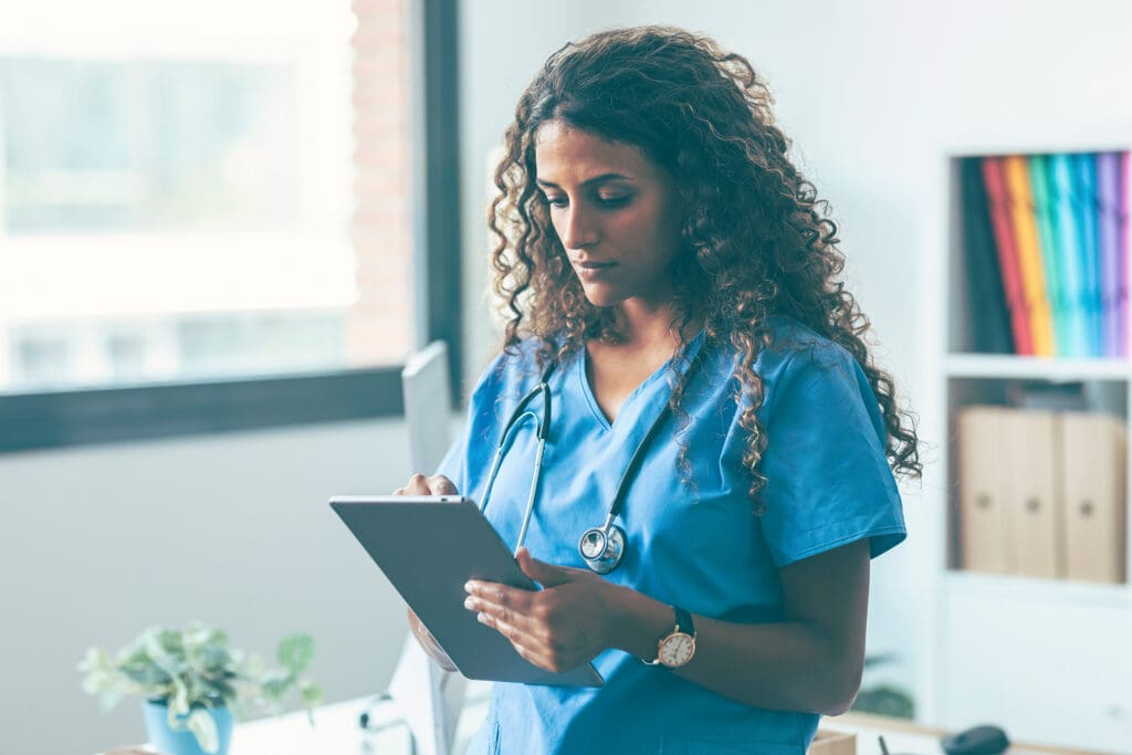 NHS clinician reviewing electronic patient records on a tablet in a medical workspace, illustrating digital healthcare, workflow efficiency, and technology‑driven care delivery.
